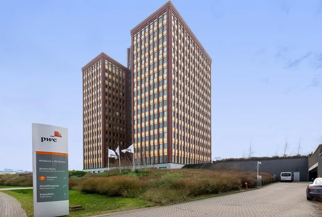 Twee hoge kantoorgebouwen van PwC aan de Fascinatio Boulevard in Rotterdam met vlaggen en bewegwijzering op de voorgrond.
